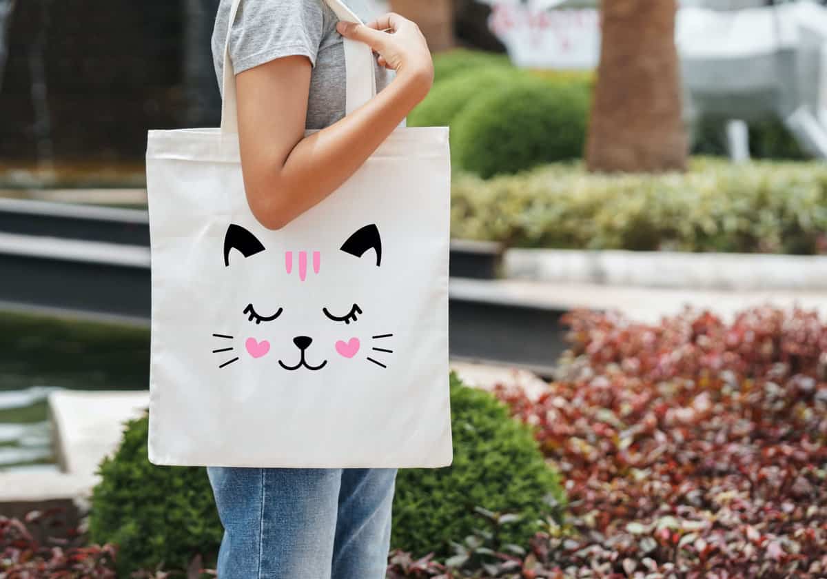 A girl holding a tote bag with a cat face on it.
