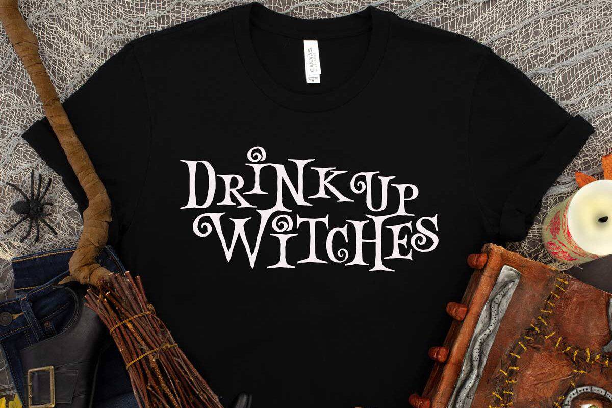 Black t-shirt with a white design that reads 'drink up witches'.