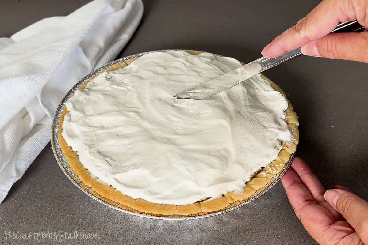Cutting into a banana cream pie with a knife.