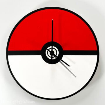 Round wall clock designed like a Poké Ball, with a red top half, white bottom half, black center circle, and black clock hands.