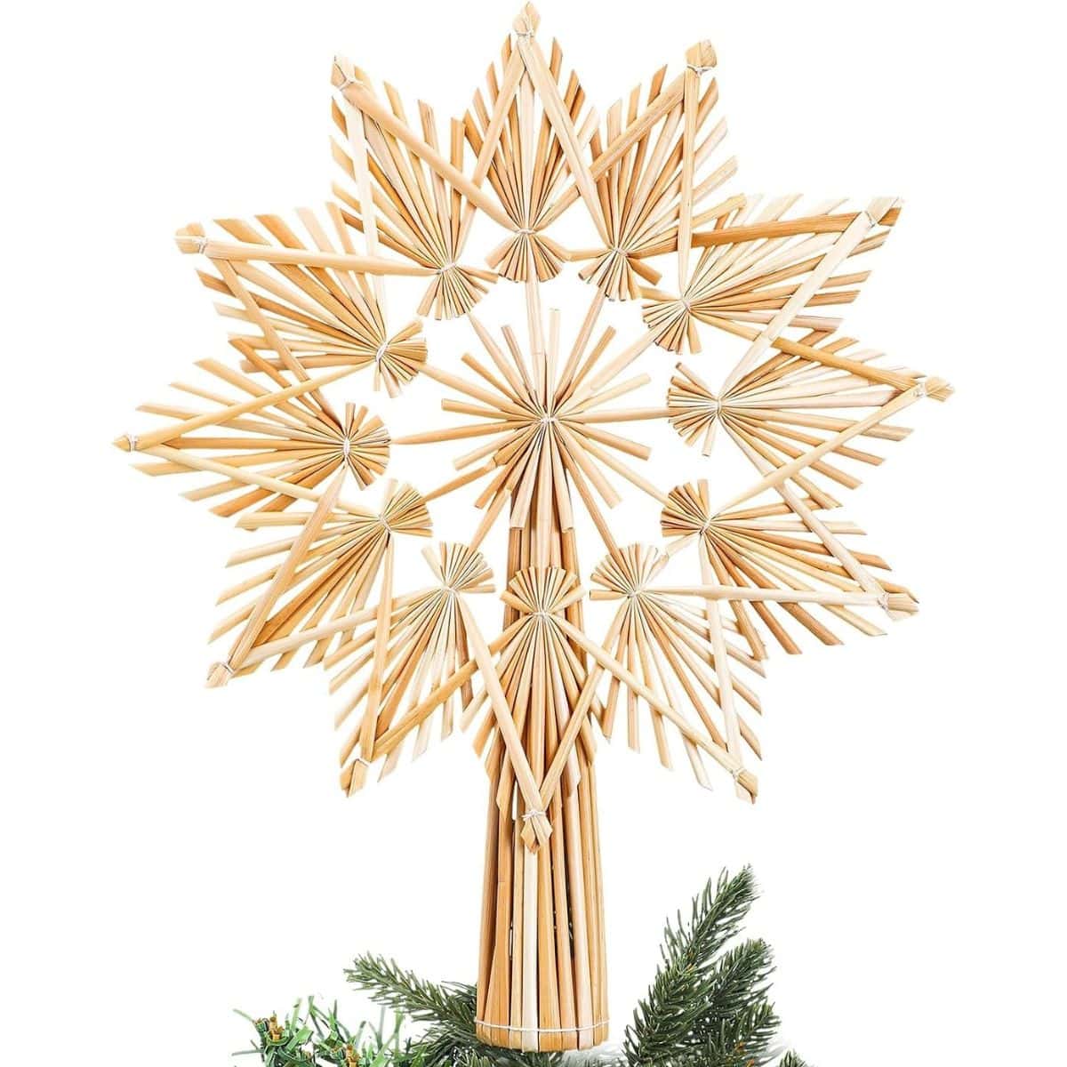 Natural straw Christmas tree topper with an eight-point star design, woven straw details, and a tall straw base resting on green tree branches.