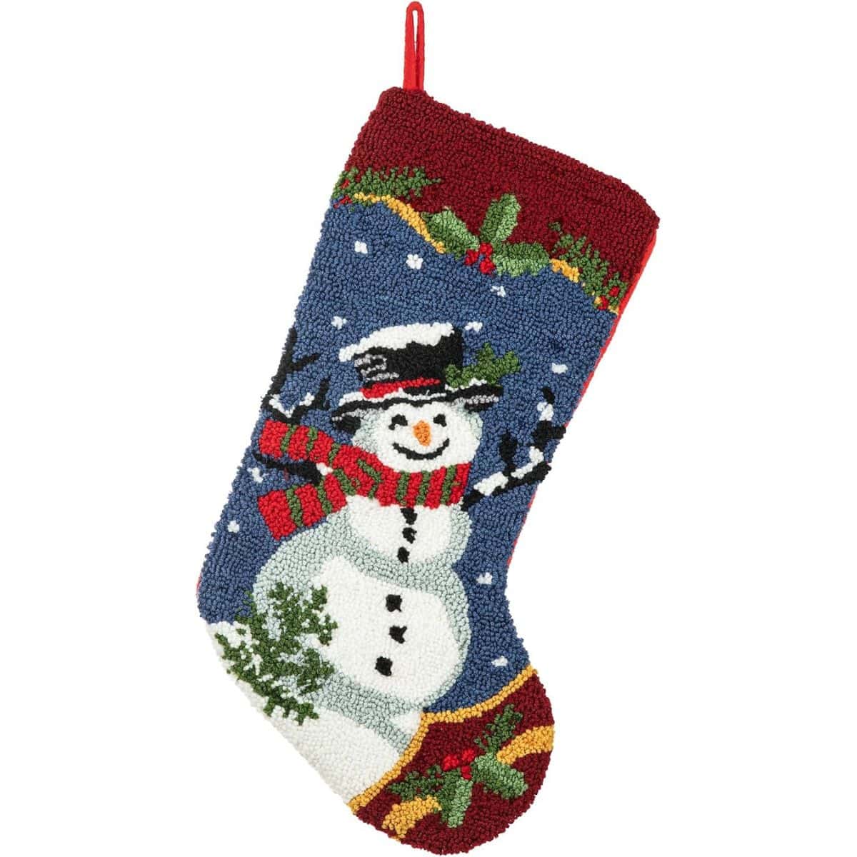 Christmas stocking with a hooked snowman design, red cuff and toe, holly accents, falling snow, and a striped scarf on a light background.