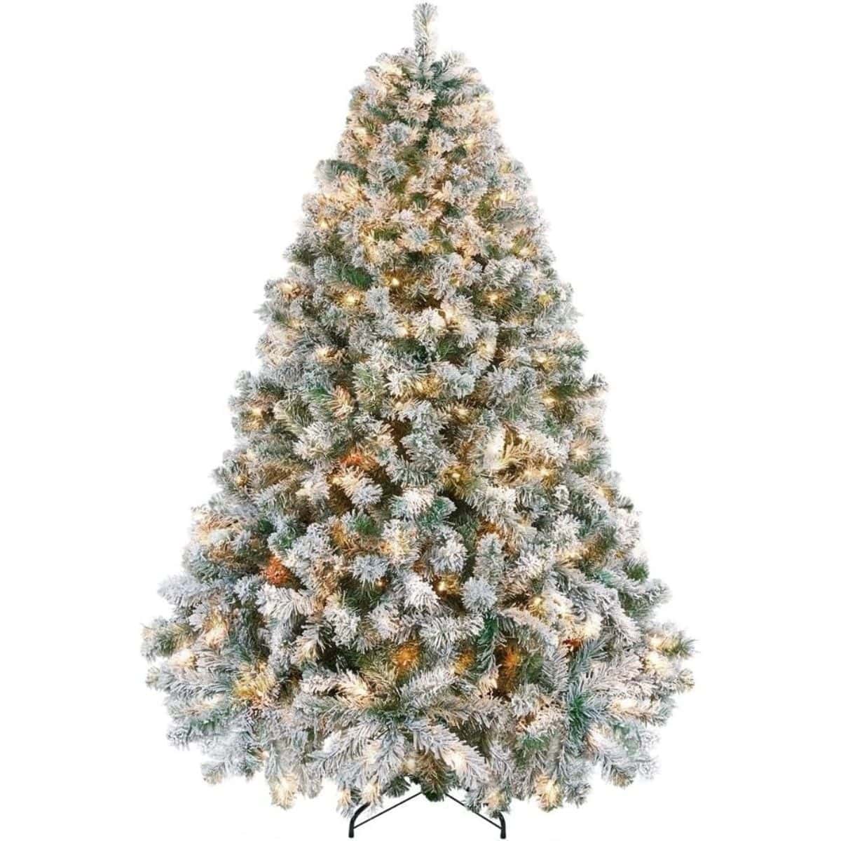 Pre-lit snow-flocked Christmas tree with full, frosted green branches, warm white lights, and a black metal stand.