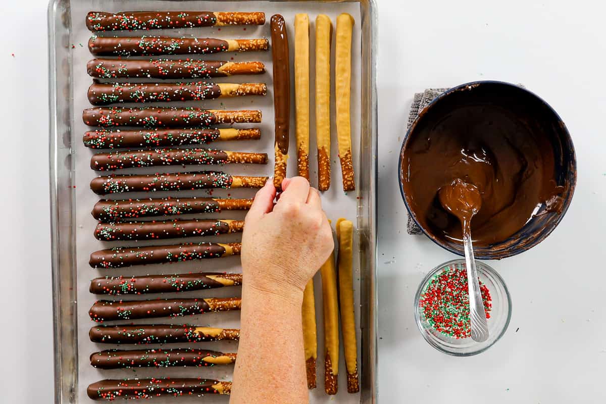 Covering pretzel sticks with dark chocolate and sprinkles.