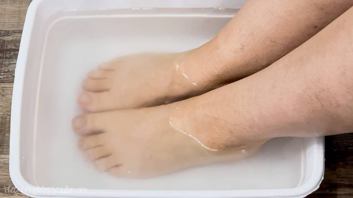 Both feet soaking in cloudy water inside a white plastic tub filled with a homemade foot soak mixture.