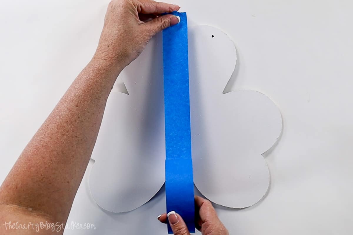 Applying painter's tape down the center of the white shamrock door hanger.