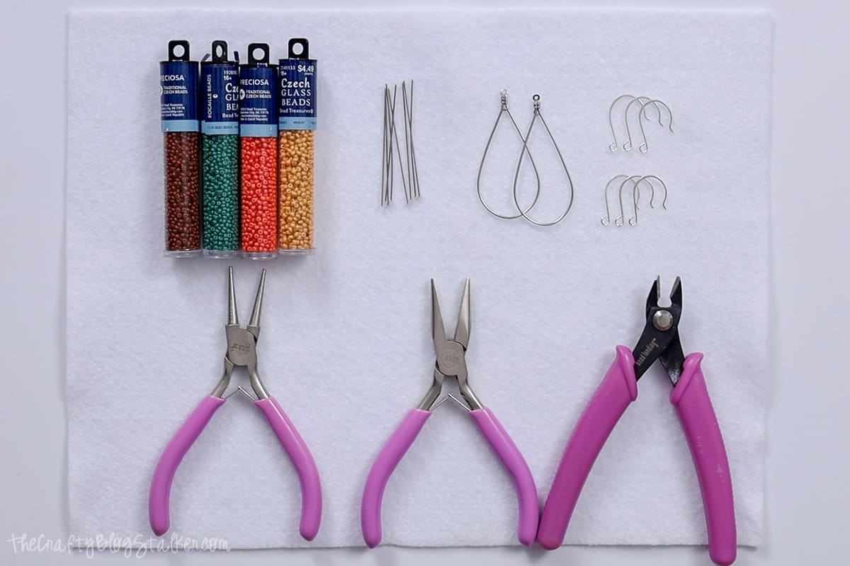 Supplies used to make seed bead earrings: jewelry pliers, seed beads, earring hooks, and head pins.
