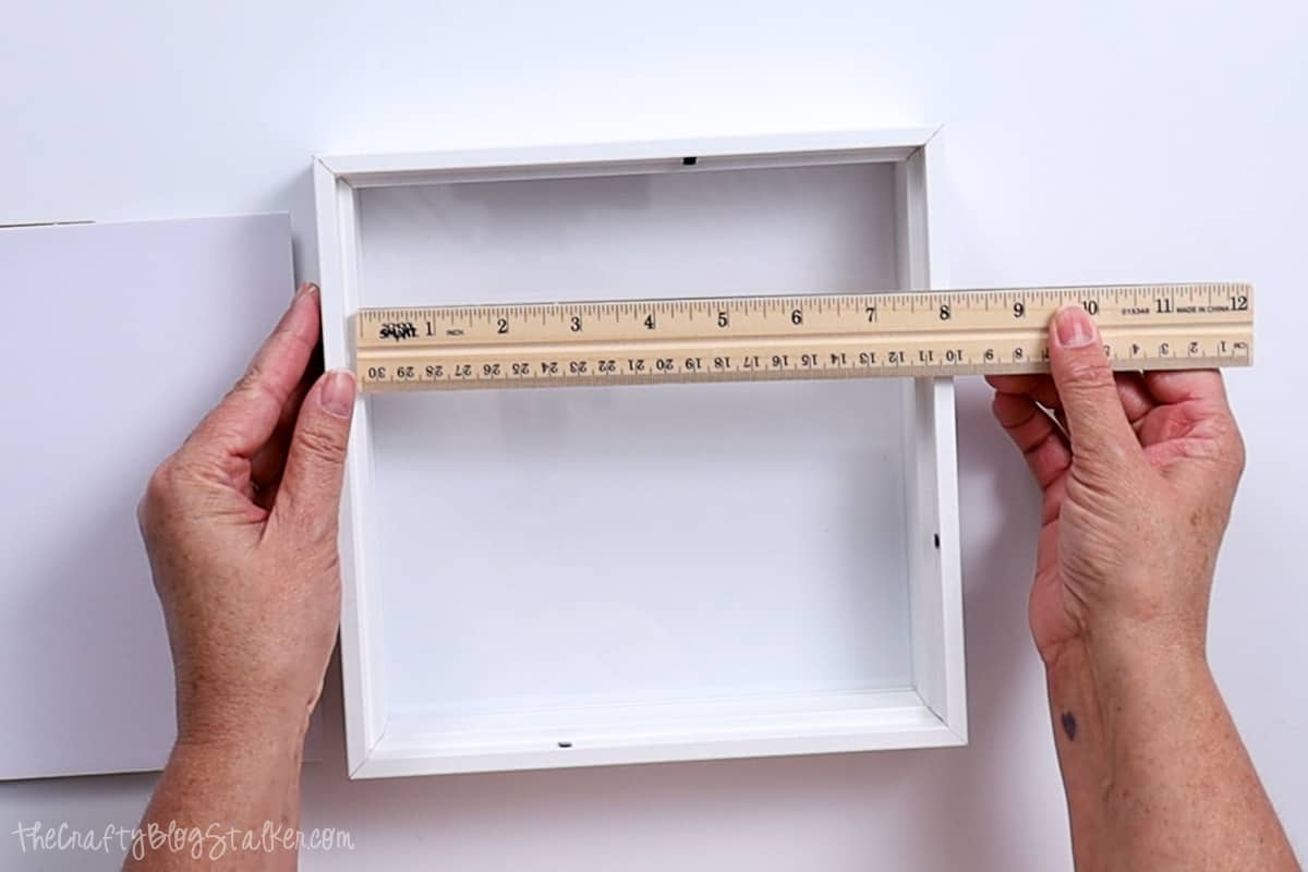 Measuring an 8x8 shadowbox frame with a ruler.