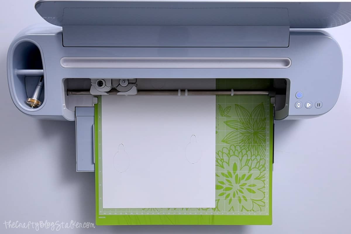Cricut cutting the design out of white cardstock.