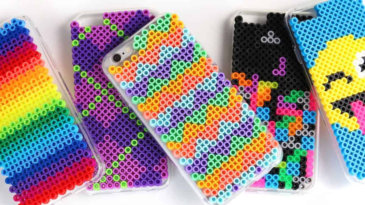 Colorful DIY Perler bead phone cases with rainbow, geometric, and emoji designs displayed on a white background.