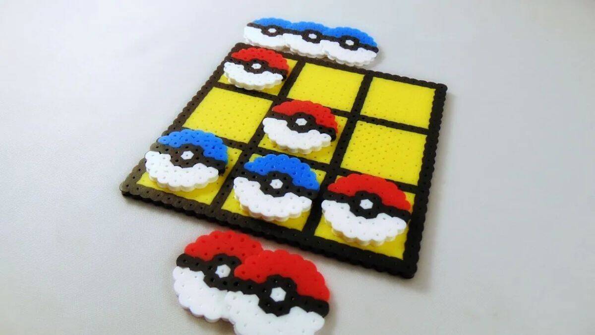 DIY Pokémon tic-tac-toe game made from Perler beads with red and blue Poké Ball pieces on a yellow game board.