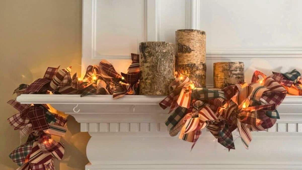 A white mantel decorated with a lighted fabric garland made of plaid and striped ribbons, paired with birch log accents for a cozy rustic look.