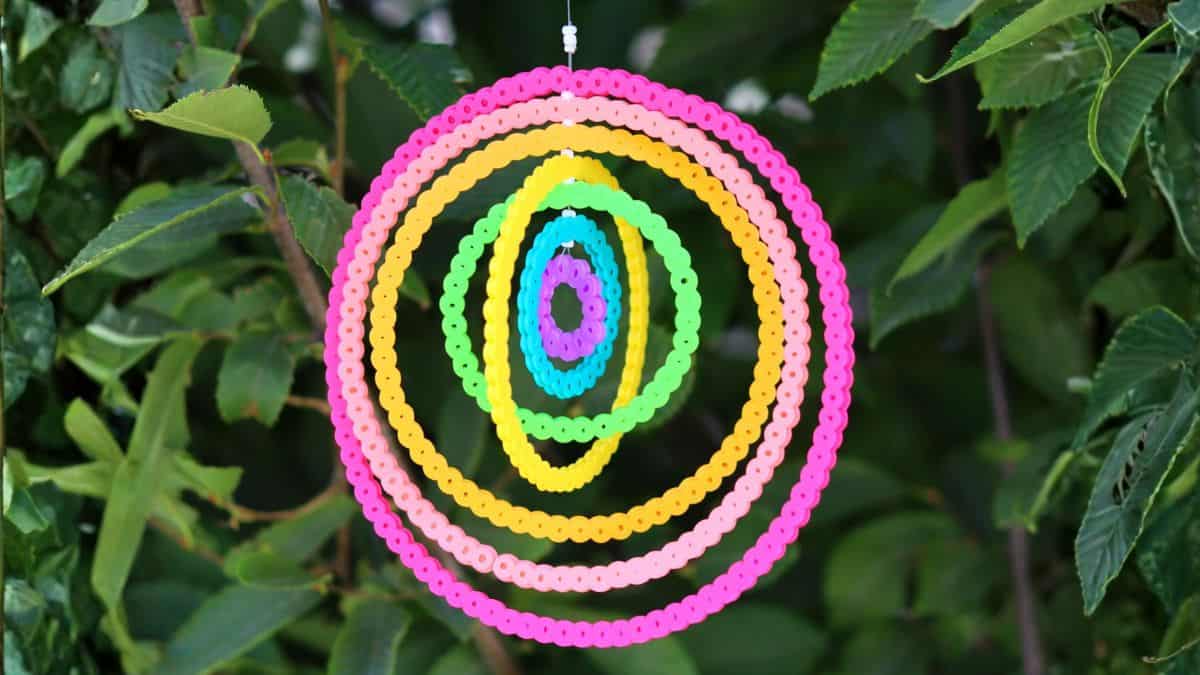 Colorful concentric circles made from Perler beads hanging outdoors in front of green leaves as a fun DIY craft decoration.