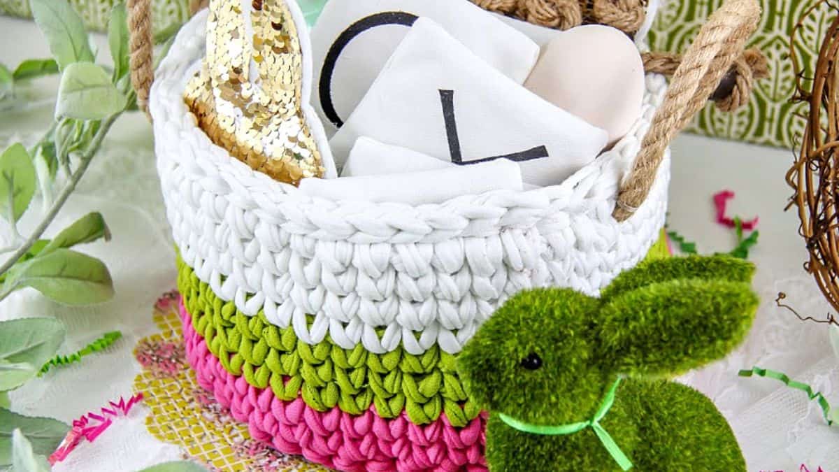 Colorful crochet Easter basket made from t-shirt yarn in pink, green, and white, filled with gifts and decorated with a green moss bunny.