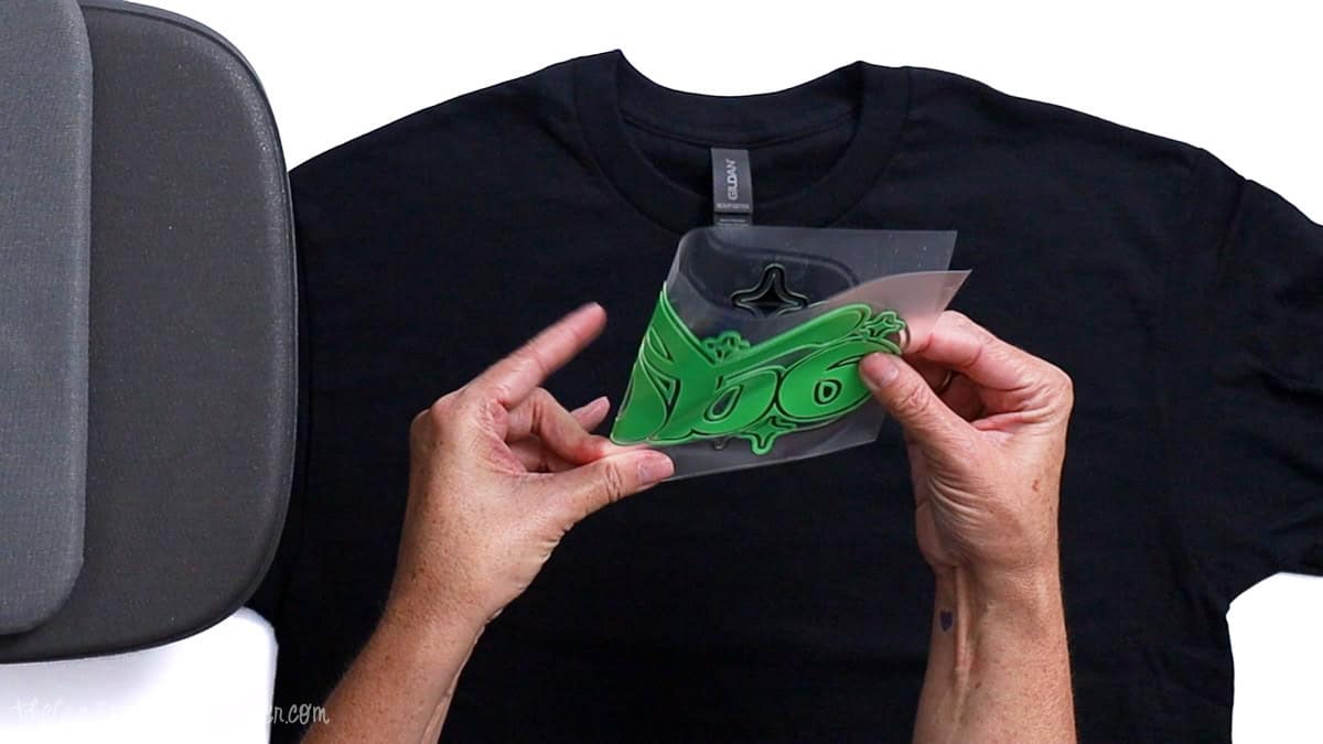 Hands folding a vinyl decal in half to find the center point before placing it onto a T-shirt for heat transfer.