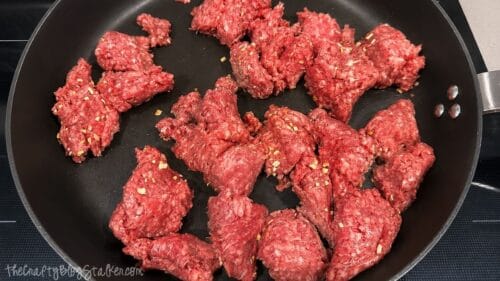 Raw ground beef cooking in a skillet with taco seasoning, ready to be browned for homemade loaded taco fries.
