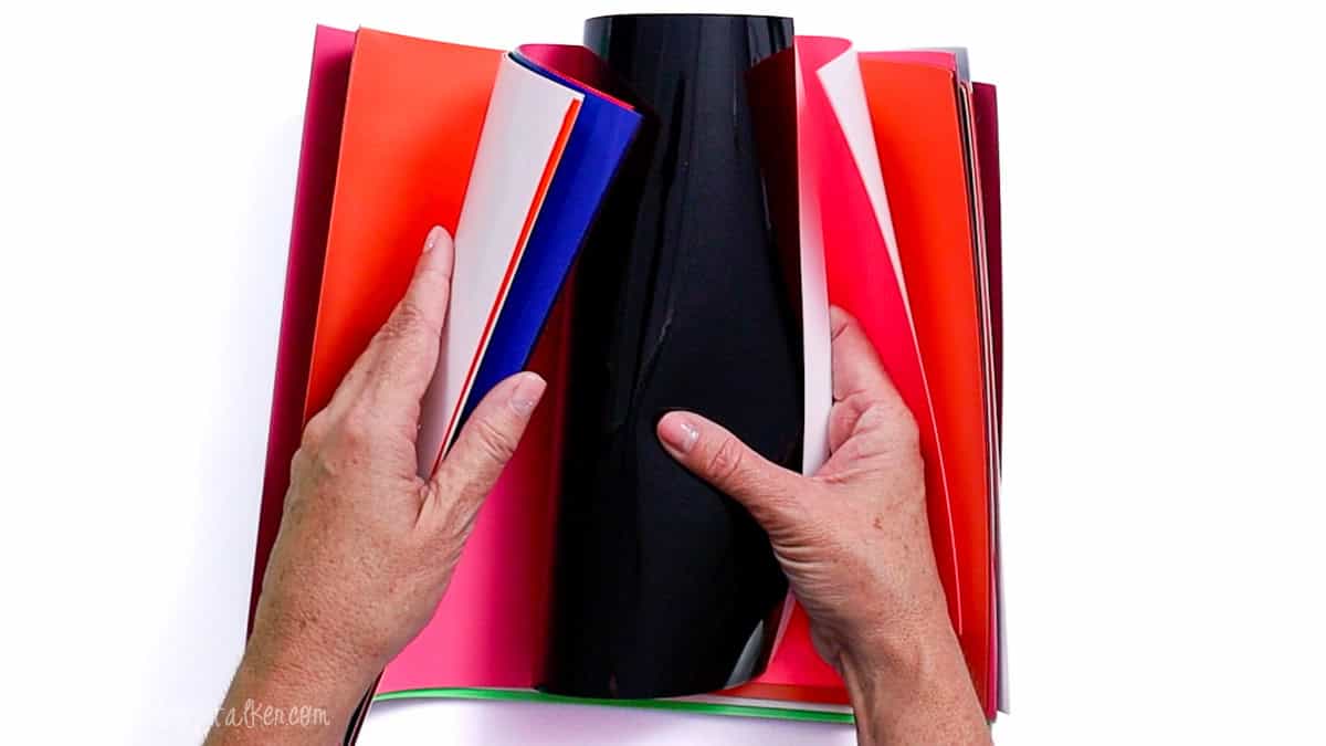 Hands flipping through a stack of assorted Super Pop heat transfer vinyl sheets in various color schemes.