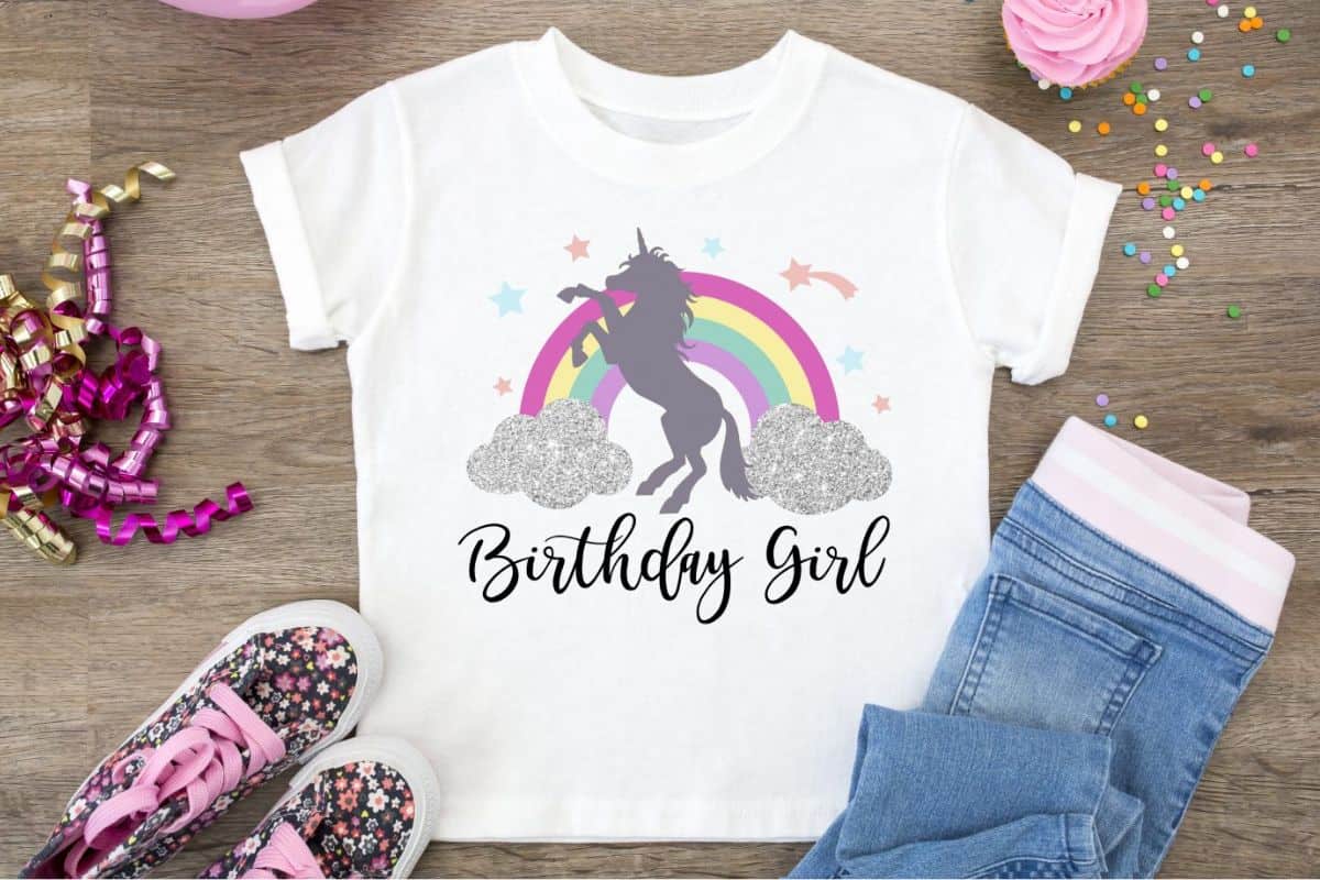 White t-shirt with a design of a rainbow and unicorn that reads 'Birthday Girl'.