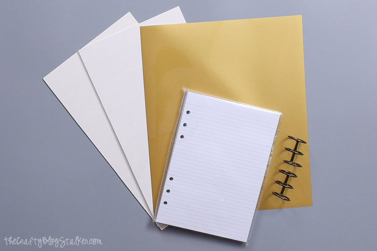 1/16 white painted basswood, gold heat transfer vinyl, A5 lined notebook paper, and two 3-ring hinged clips.