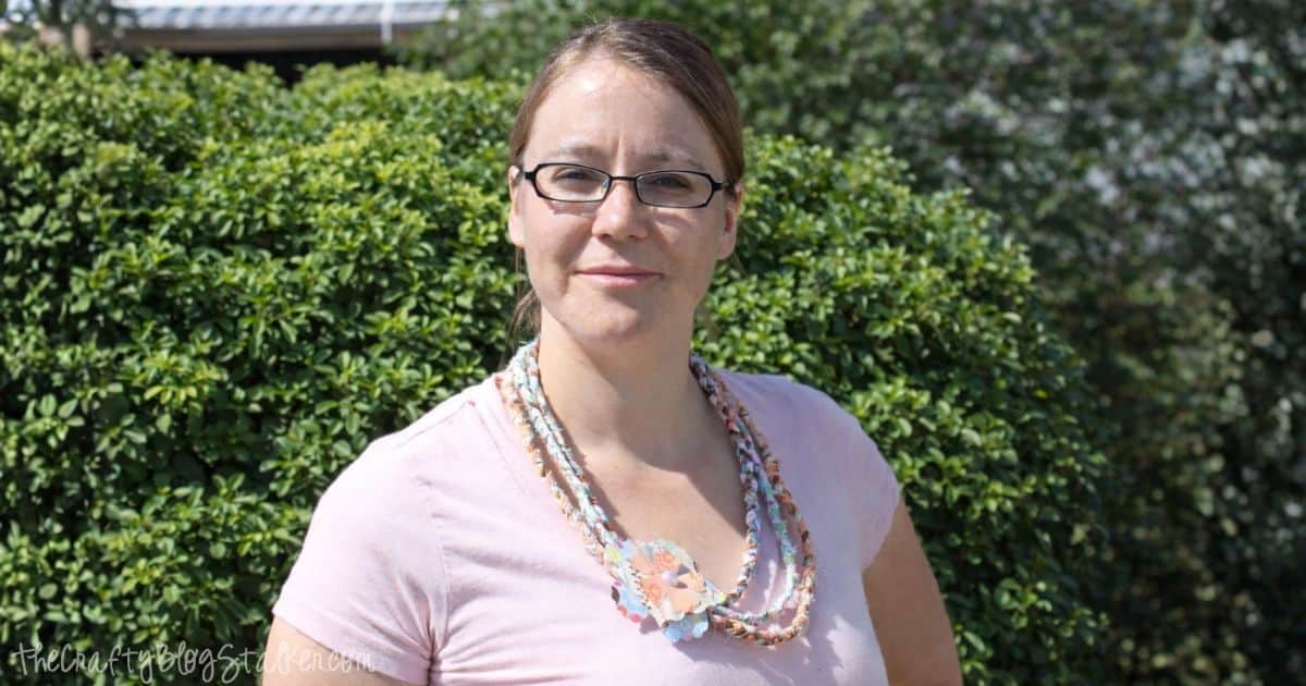 Close-up view of a no-sew braided fabric necklace featuring colorful fabric scraps and a layered fabric flower with a pearl center, adding a handmade touch to a casual outfit.