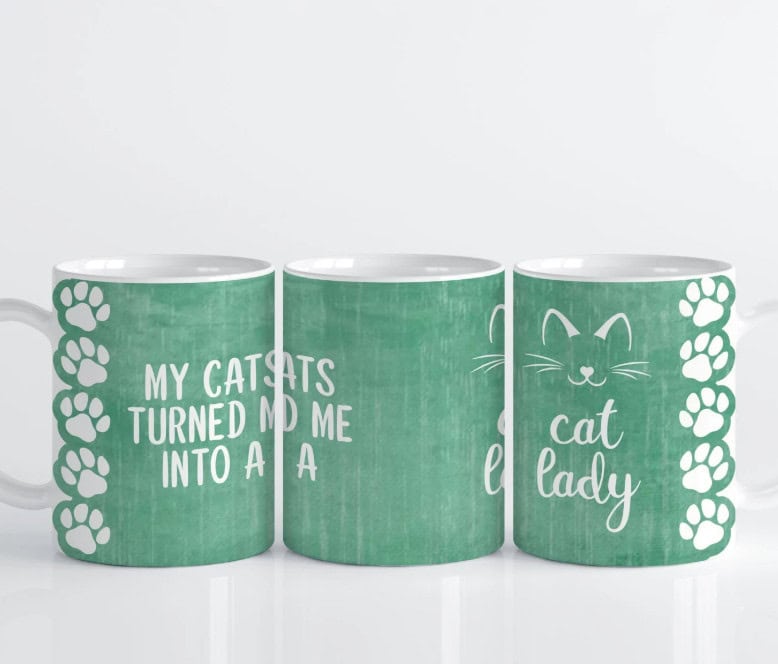 Set of three green mugs with white text and paw print designs. The text reads, "My cats turned me into a cat lady," accompanied by a simple cat face illustration.