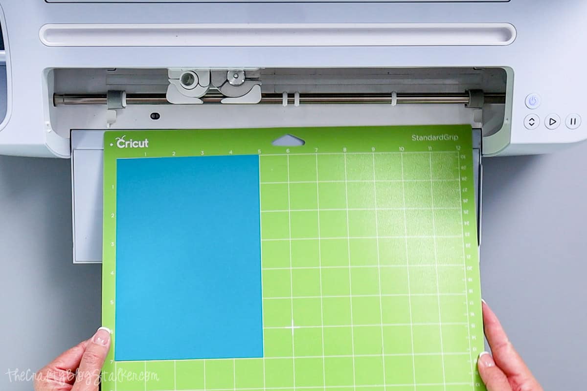Hands loading a Cricut StandardGrip mat with blue cardstock into a Cricut cutting machine, preparing to cut a circle out of cardstock.