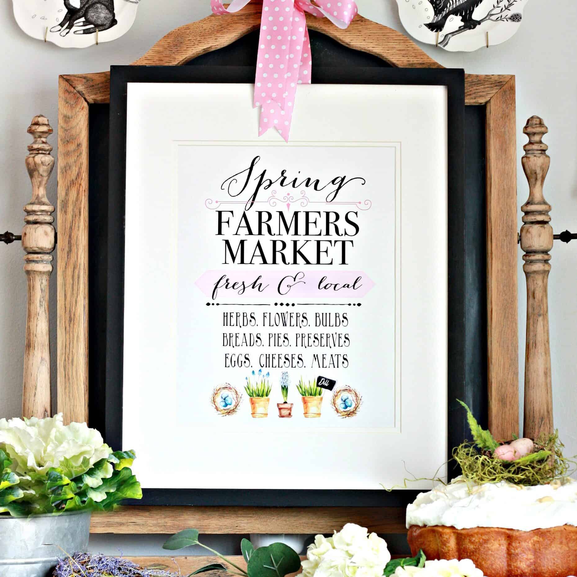 Spring Farmers Market printable in a rustic frame with a pink ribbon, surrounded by fresh flowers, greenery, a bird’s nest with eggs, and a cake on a stand.