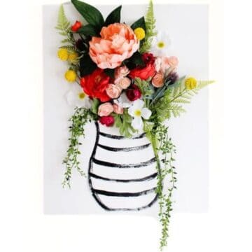 DIY canvas wall art featuring a painted striped vase with colorful artificial flowers and greenery arranged to look like a 3D bouquet overflowing from the top