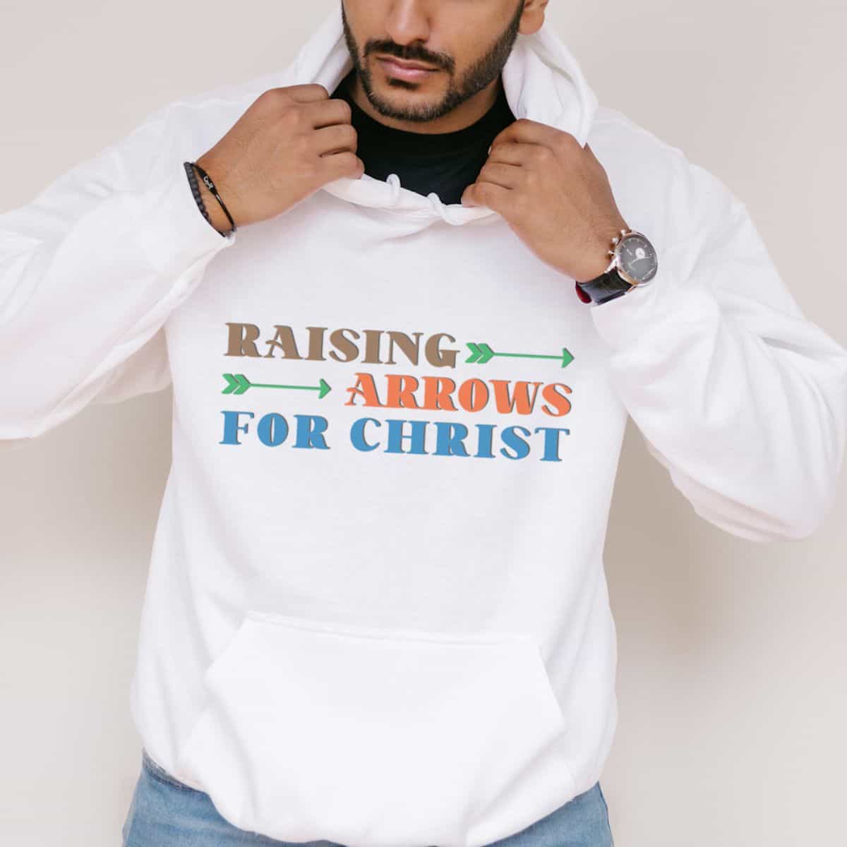 Man wearing a white hoodie with colorful text and arrows that reads "Raising Arrows for Christ" in brown, orange, green, and blue lettering.