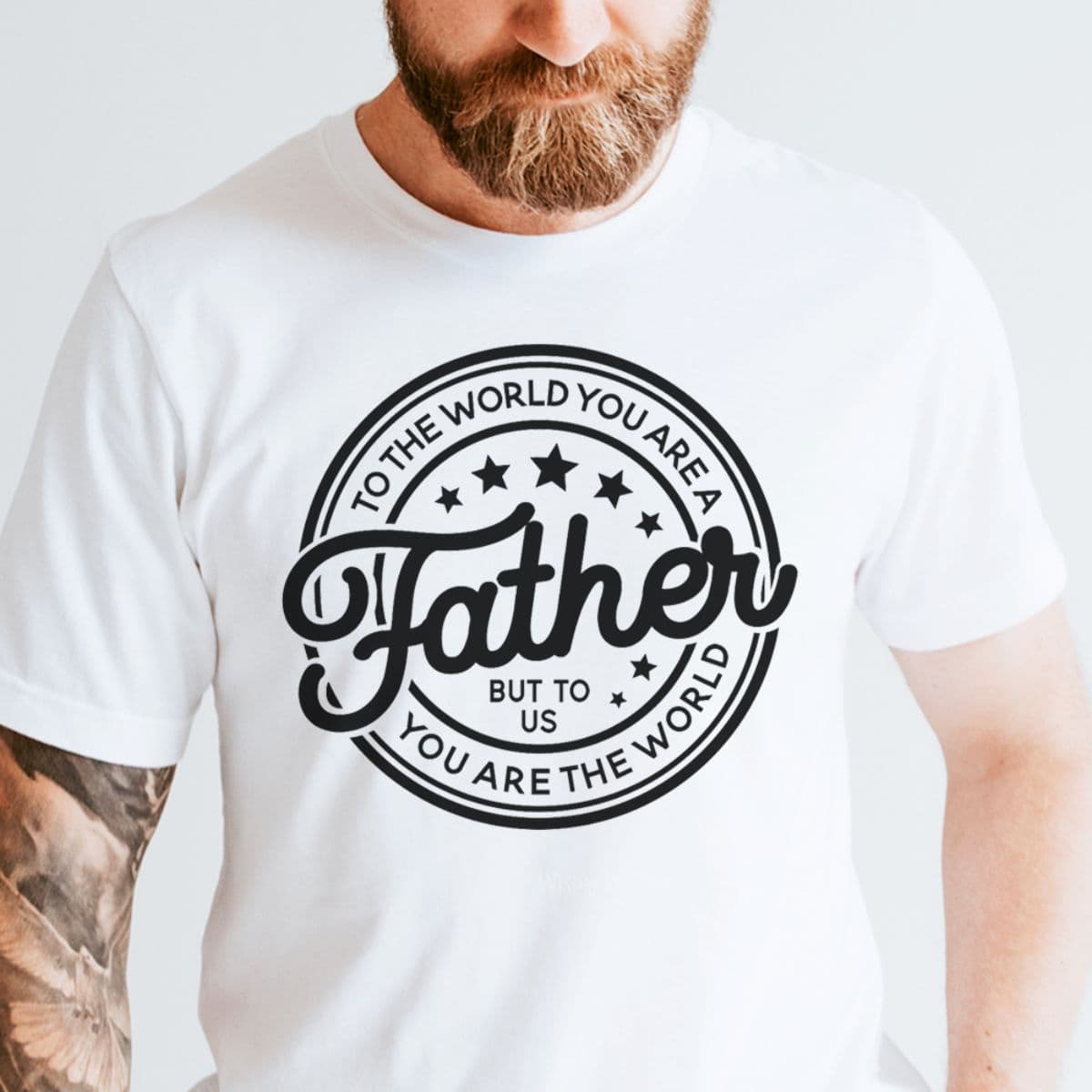 Man wearing a white t-shirt with a circular black design that says, "To the world you are a Father, but to us you are the world," surrounded by stars.