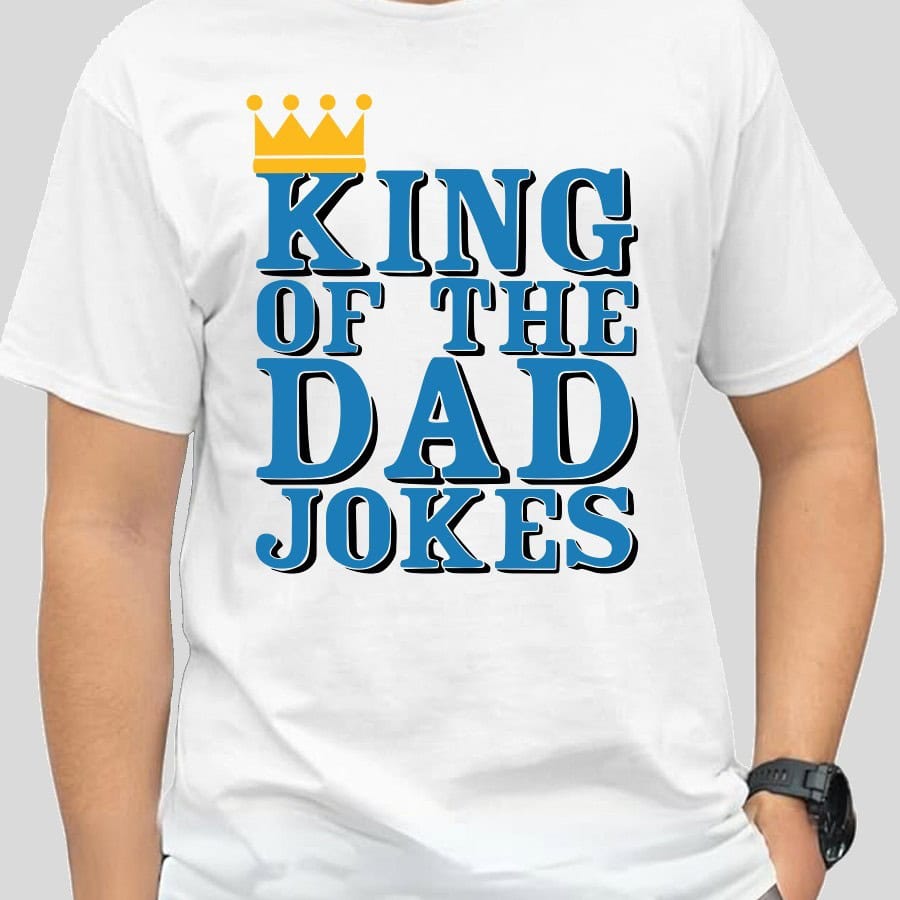 Man wearing a white t-shirt with a bold design that reads "King of the Dad Jokes" in blue and black text, topped with a yellow crown graphic.