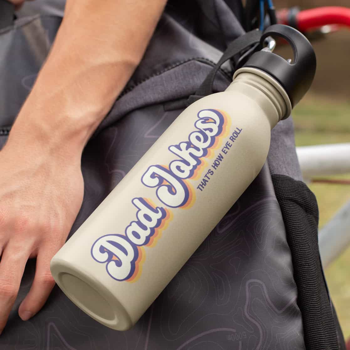 Beige water bottle clipped to a backpack with retro-style text that reads “Dad Jokes” and smaller text saying “That’s how eye roll.”