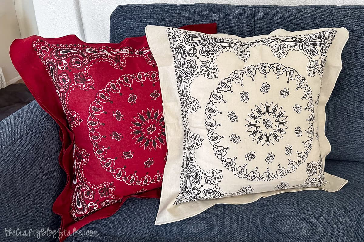Two decorative bandana pillows, one red and one cream, sit side by side on a blue couch, showcasing a stylish DIY home decor project.