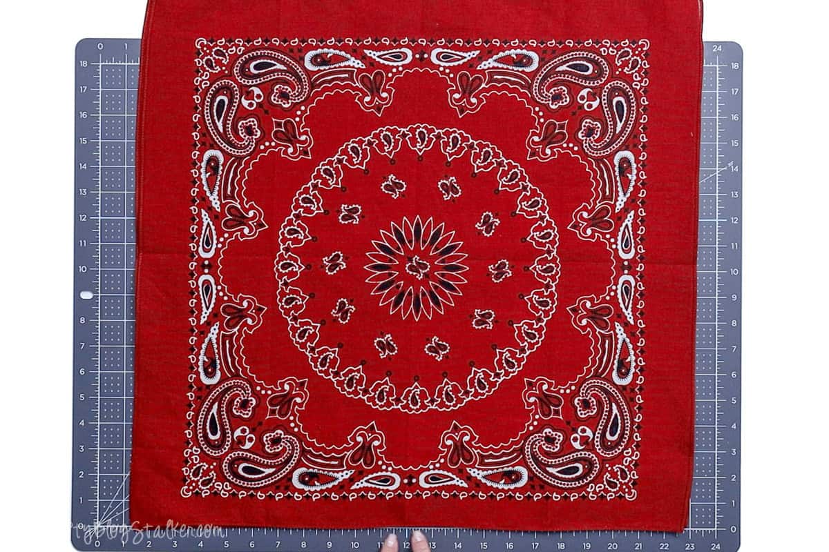 Two red bandanas layered together on a cutting mat, showing a centered paisley and floral design in white and black, ready to be sewn into a pillow.