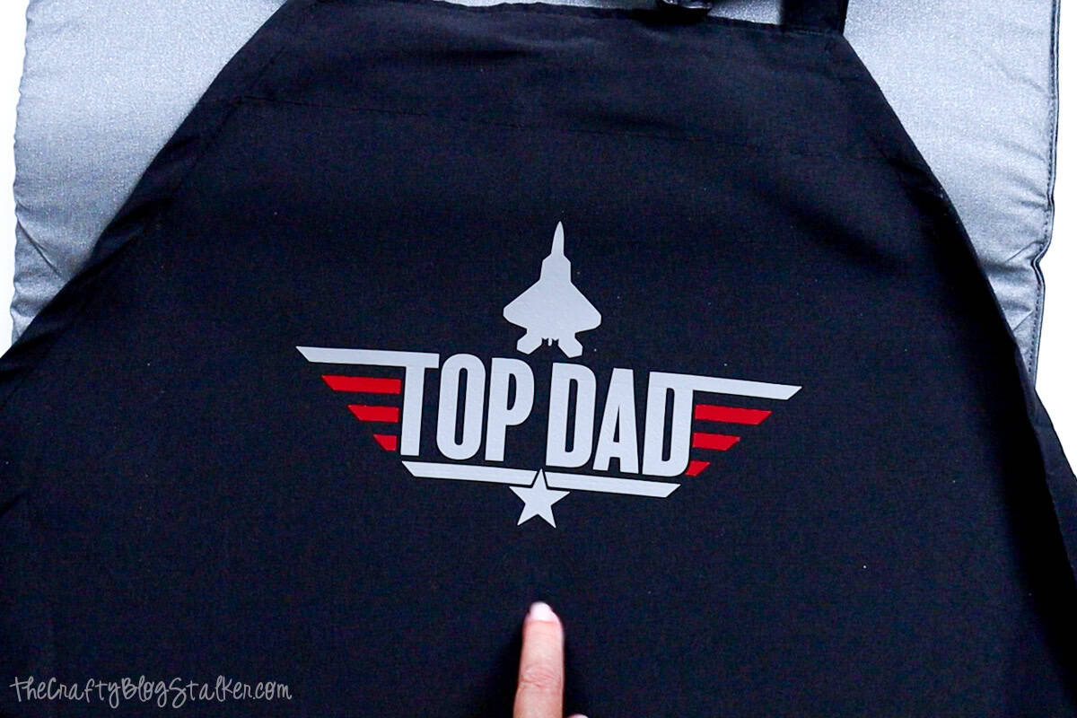 Finished black apron with a smooth “Top Dad” vinyl design featuring a jet and red wing stripes, shown wrinkle-free and centered on the apron front.