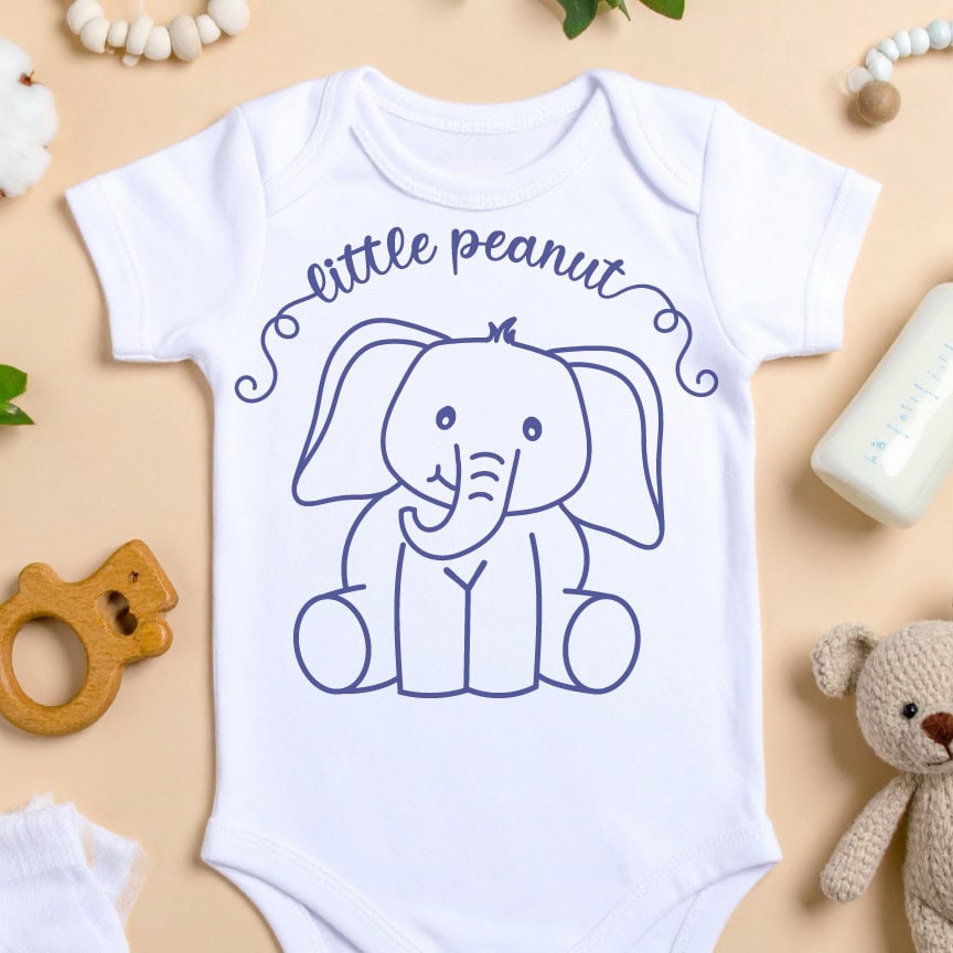 White baby onesie with a cute navy line drawing of a baby elephant and the phrase “little peanut” above it, surrounded by baby items on a neutral background.
