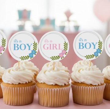Vanilla cupcakes with white frosting topped with round “It’s a Boy” and “It’s a Girl” cupcake toppers featuring floral designs, perfect for a baby shower.