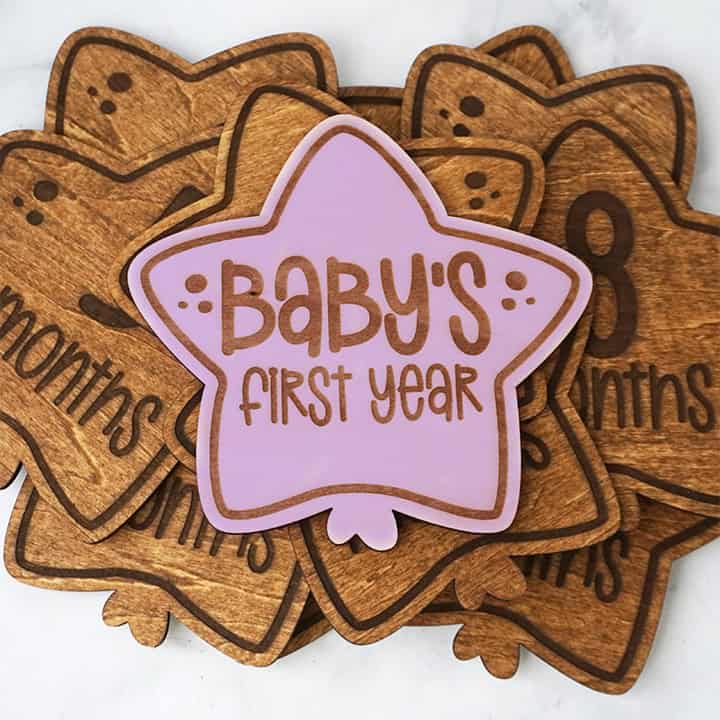 Wooden milestone markers shaped like balloons, with a pink star reading "Baby's First Year" on top of monthly markers for tracking a baby's growth.