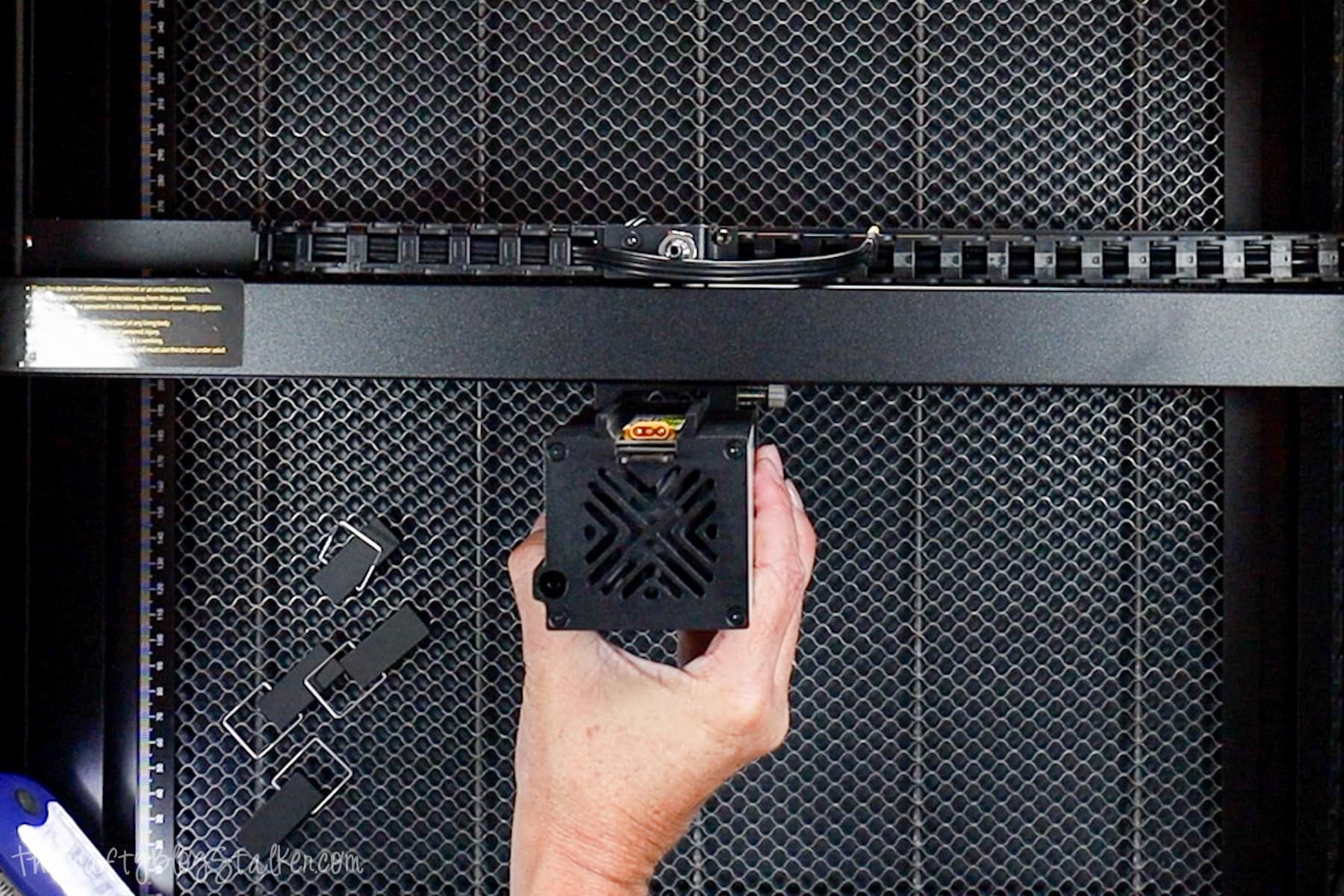 Hand installing the Acmer P3 laser module onto the slider rail inside the engraver, with the honeycomb cutting bed and metal clamps visible below.
