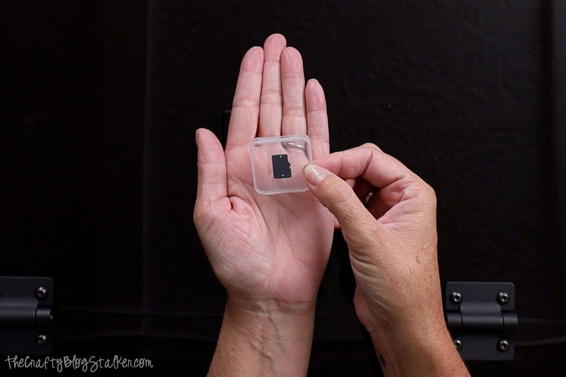 Hands holding a small plastic case containing a TF card, used with the Acmer P3 Laser Engraver for storing and transferring design files.