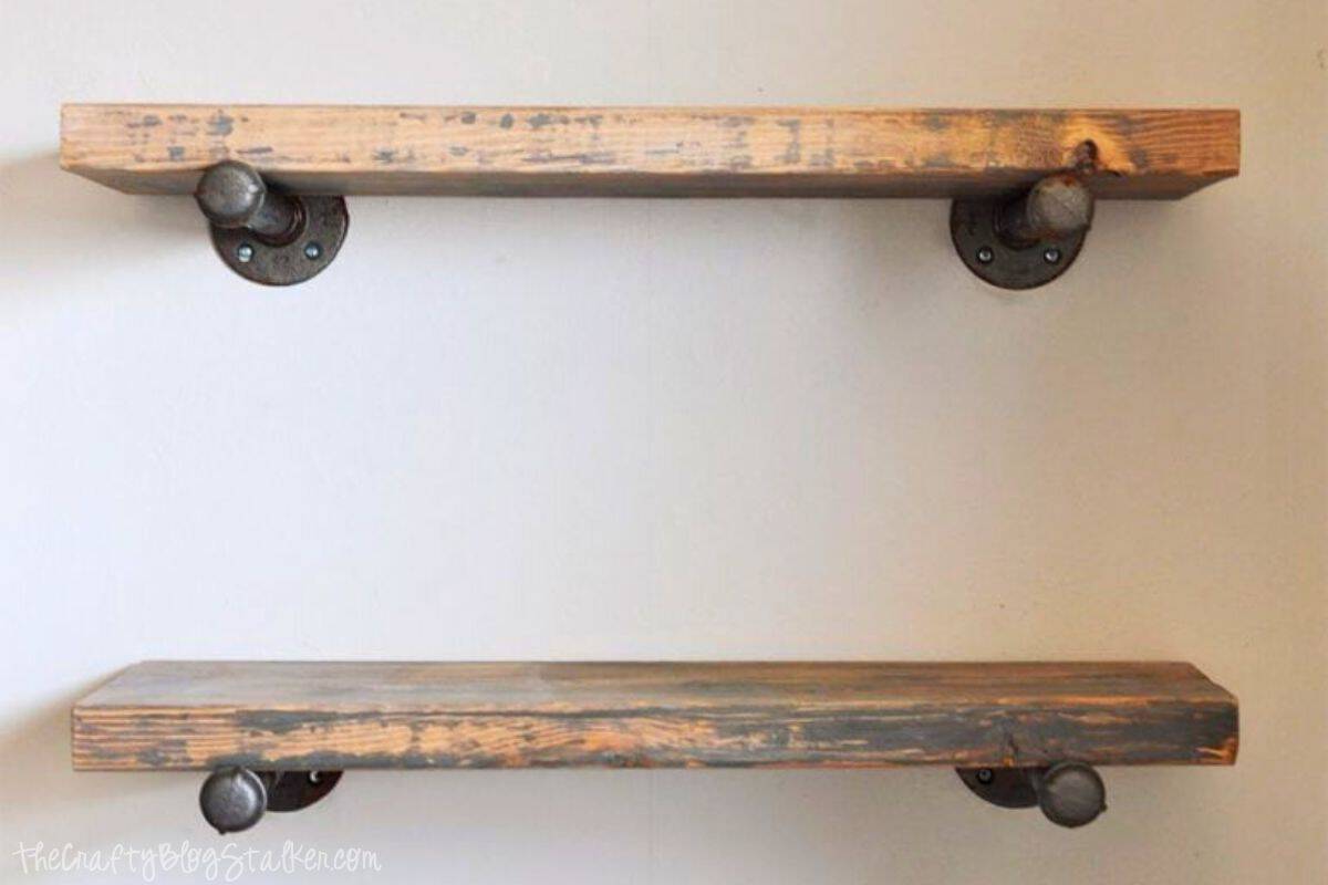 Two rustic wooden shelves mounted on a wall using industrial-style black metal pipe brackets, showcasing a simple and sturdy DIY shelf design.