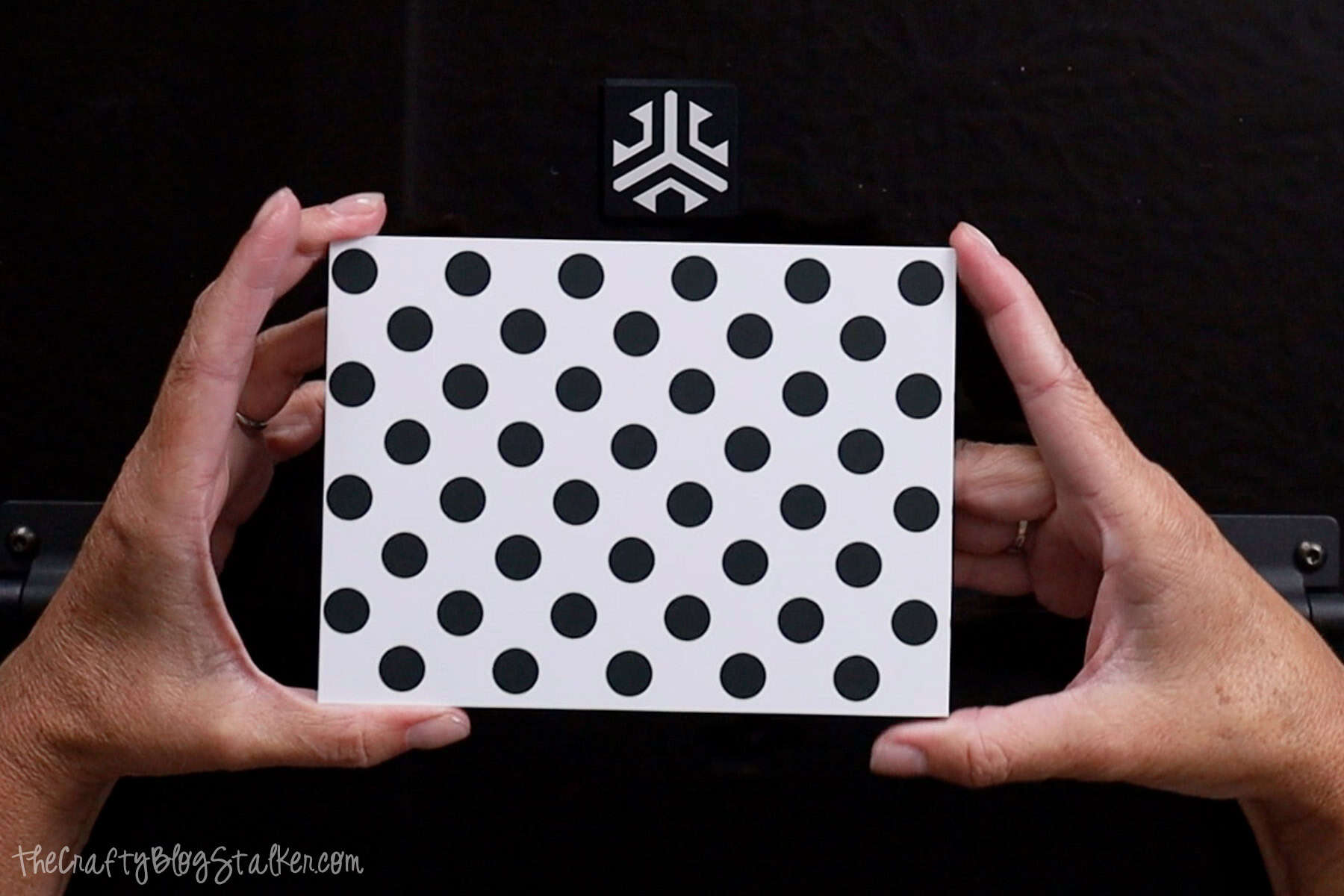 Hands holding a dotted calibration card in front of the Acmer P3 Laser Engraver, used for aligning the camera during setup in the LightBurn software.