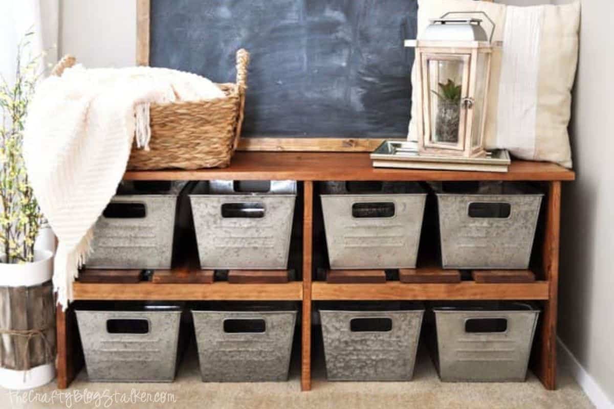 Rustic wooden entryway bench with eight galvanized metal bins for storage, topped with cozy decor including a basket, lantern, and pillow.