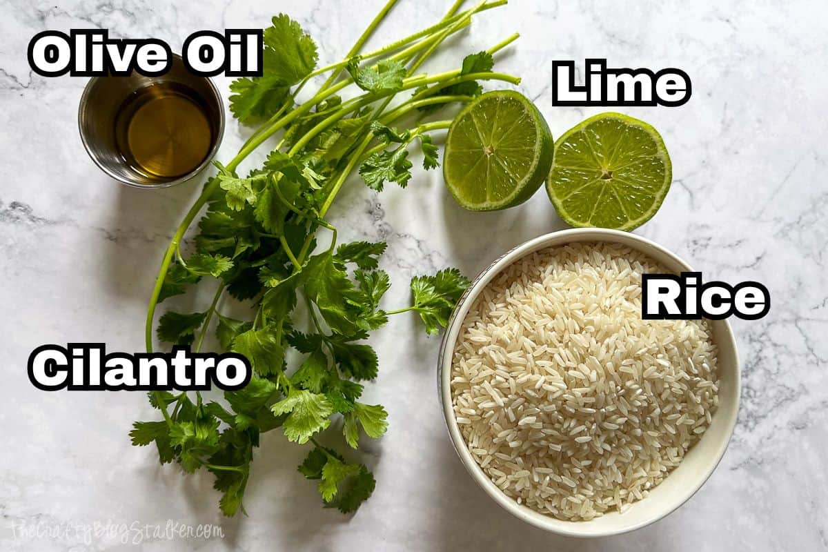 Fresh cilantro, halved limes, dry white rice, and a small cup of olive oil arranged on a marble surface, labeled as ingredients for cilantro lime rice.