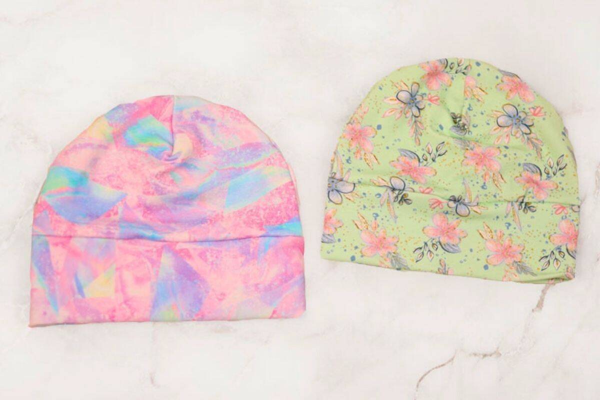 Two handmade baby hats displayed side by side: one with a pastel rainbow pattern and the other with a light green floral design.