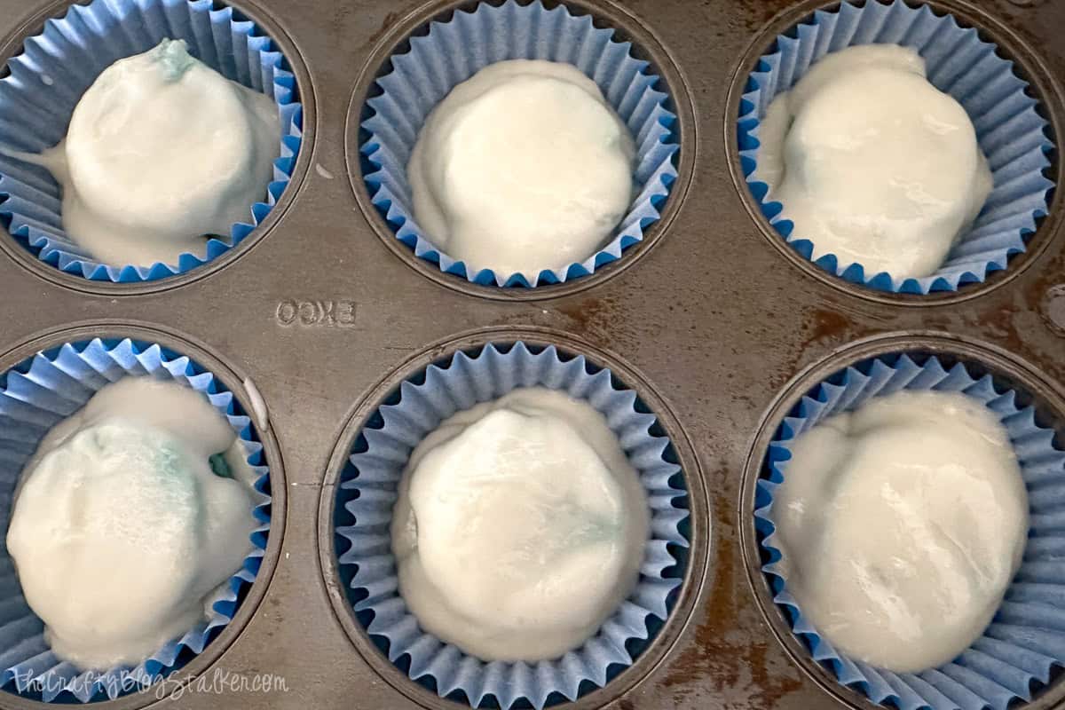 Cupcake pan filled with blue paper liners and white cake batter, ready to be baked for gender reveal cupcakes.