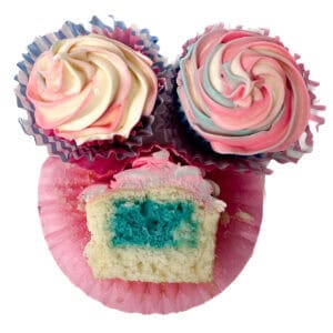 Three gender reveal cupcakes with swirled pink, blue, and white frosting; one is cut open to show a bright blue cake center.