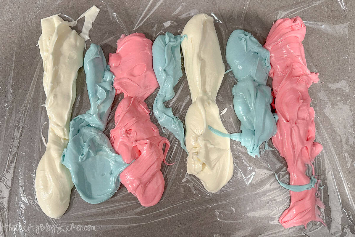 Stripes of white, pink, and blue frosting spread on plastic wrap, ready to be rolled for multicolor piping on cupcakes.