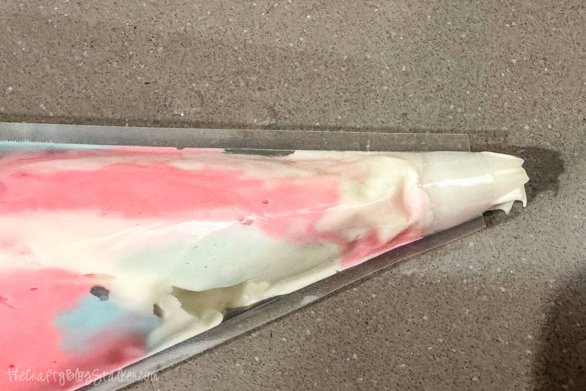 Piping bag filled with swirled pink, blue, and white frosting, ready to decorate cupcakes with a colorful reveal design.