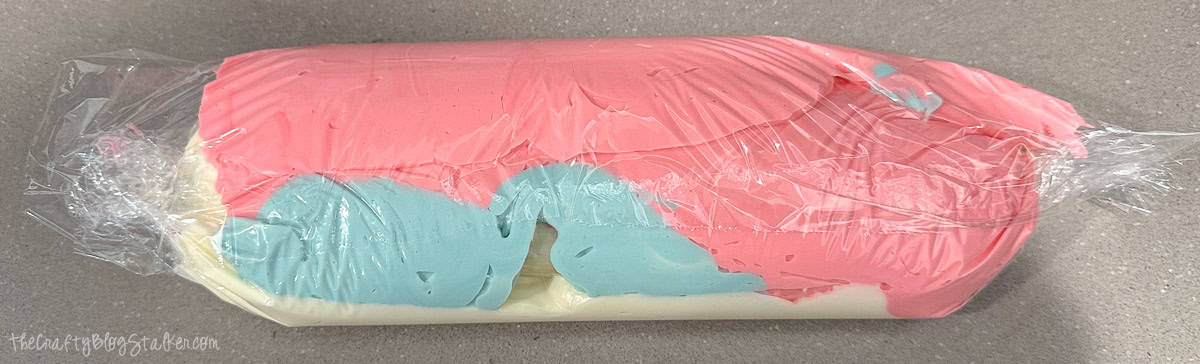 Rolled plastic wrap filled with stripes of pink, blue, and white frosting, prepped for piping multicolor swirls on cupcakes.